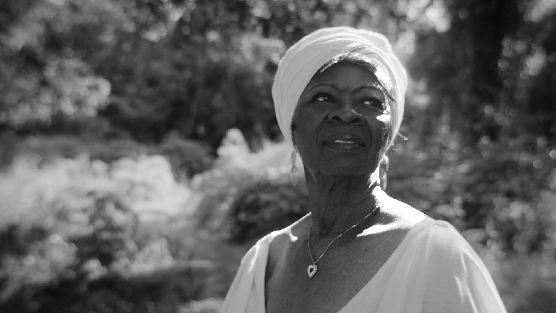 Irma Thomas in a white headwrap, looking up, in a sunlit garden